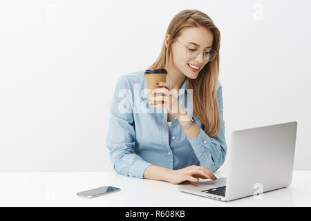 Girl sitting in cafe travaillant en freelance, ordinateur portable parlant à client, de boire du café à partir de la tasse de papier et souriant heureux avec beaucoup de succès en soupirant Banque D'Images