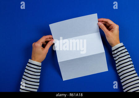 Femme hands holding blank white flyer brochure brochure. Modèle de fiche maquette brochure publicitaire sur fond bleu Banque D'Images