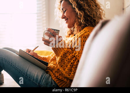 Happy cute lady at home écrire des notes sur un journal tandis que boire une tasse de thé et se reposer et se détendre en vacances, couleurs de l'automne et les personnes bénéficiant de la vie à la maison Banque D'Images