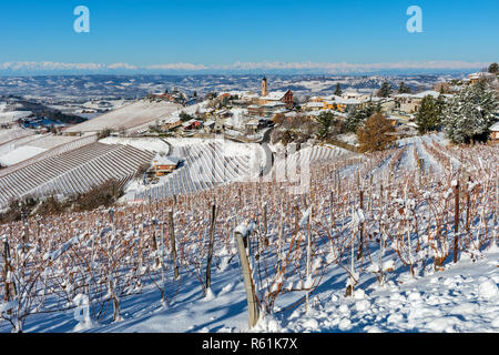 Vue sur vignes et collines enneigées sur la petite ville de Treiso sur l'arrière-plan sous ciel bleu en Piémont, Italie du Nord. Banque D'Images