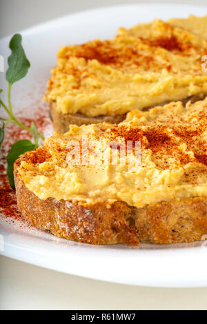 Deux sandwiches ouverts d'hummus et paprika en poudre sur une assiette blanche - verticale vue rapprochée Banque D'Images