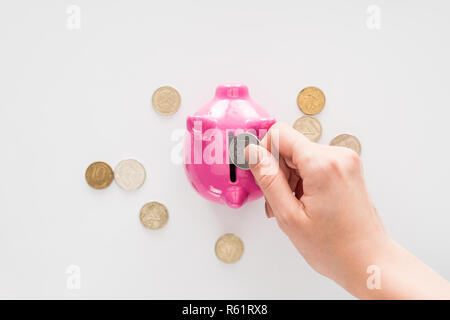 Portrait of woman putting coins en pink piggy bank on white surface Banque D'Images