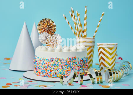 Gâteau, chapeaux de fête, vinyl, tasses de papier doré et de banderoles pailles sur fond bleu avec confetti Banque D'Images