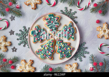 Les biscuits de Noël en forme d'arbres de Noël et des flocons de neige avec des branches de sapin, des cannes de bonbon et de baies sur fond clair, de mise à plat Banque D'Images