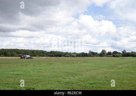 Tracteur agricole rouge sur le côté gauche dans un domaine agricole avec un bleu ciel nuageux. Banque D'Images