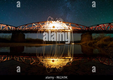 La lumière peinture art concept. La filature de la laine d'acier en résumé, cercle de douches d'artifice lumineux jaune vif brille sur long pont reflète dans riv Banque D'Images