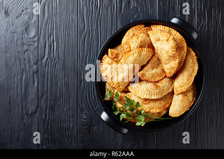 Vue de dessus de chebureki ou en friture chaussons avec une masse de remplissage de la viande bovine et l'oignon dans une cocotte noire sur une table en bois, vue d'abo Banque D'Images