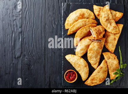 Chiffres d'frits délicieux ou chebureki viande hachée avec l'oignon et les herbes en remplissant une plaque de pierre noire sur une table en bois, d'un point de vue horizontal Banque D'Images