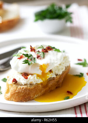 Toasts de pain croustillant avec du fromage cottage, oeuf poché et tomates séchées sur un fond clair. Banque D'Images