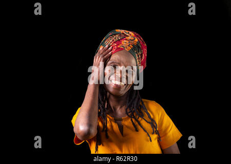 Libre d'une vieille femme africaine souriant et portant un foulard sur un fond noir Banque D'Images