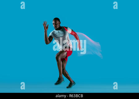 Portrait de jeunes active musculaire de l'Afrique de l'homme courant, isolé sur fond studio bleu avec des éclairs de lumière Banque D'Images