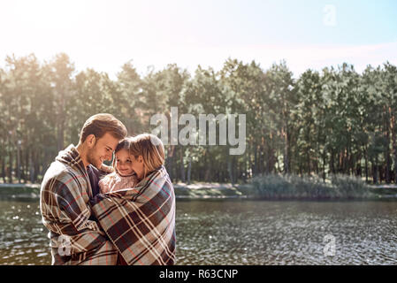 Les jeunes parents hugg leur petite fille dans la forêt d'automne près du lac. Banque D'Images