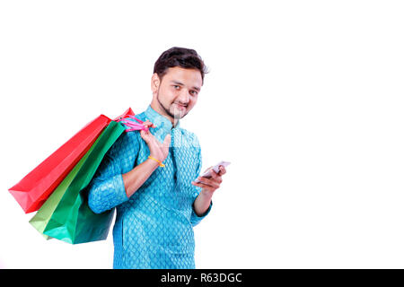 L'homme indien ethnique dans l'usure avec les sacs et montrant l'écran mobile isolé sur fond blanc , Banque D'Images