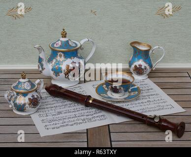 Verre d'anglais avec soucoupe, théière, sucrier et pot à crème, céramique fine porcelaine, et une flûte de bloc sur une feuille de musique Banque D'Images