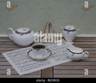 Verre d'anglais avec soucoupe, théière, pot à crème et le sucrier, céramique fine porcelaine, et d'un métronome pour la musique sur une feuille de musique Banque D'Images