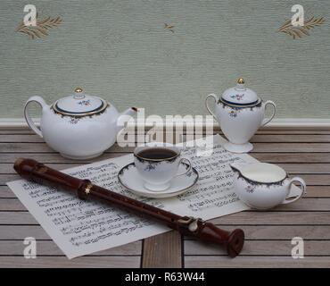 Verre d'anglais avec soucoupe, théière, pot à crème et le sucrier, céramique fine porcelaine, et une flûte de bloc sur une feuille de musique Banque D'Images