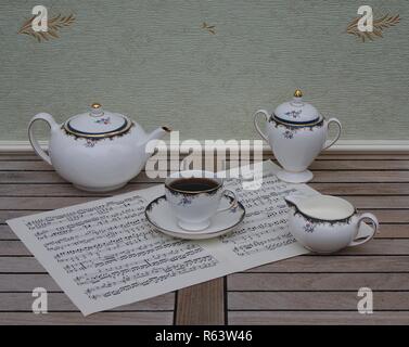 Verre d'anglais avec soucoupe, théière, pot à crème et le sucrier, céramique fine porcelaine, sur une feuille de musique Banque D'Images