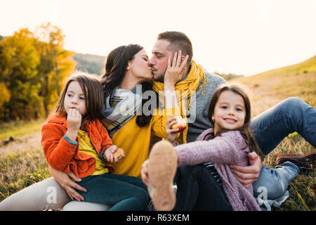 Un portrait de jeune famille avec deux petits enfants en automne nature au coucher du soleil, des baisers. Banque D'Images