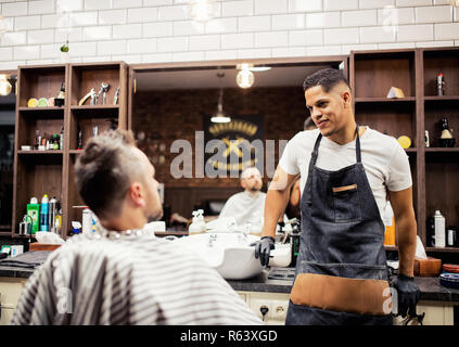 Un homme parlant à client et coiffeurs coiffeur dans un salon de coiffure. Banque D'Images