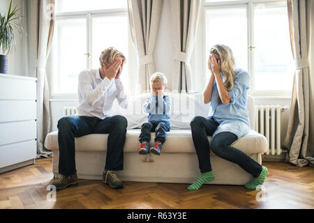 Les jeunes parents et petit garçon assis sur un canapé à l'intérieur dans une chambre à coucher, couvrant les yeux. Banque D'Images