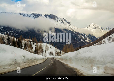 Route asphaltée sinueuse vide qui s'étend à travers la neige profonde vers belle Alpes blanc brillant woody montagne rocheuse escarpée sous les pics d'hiver nuageux Banque D'Images