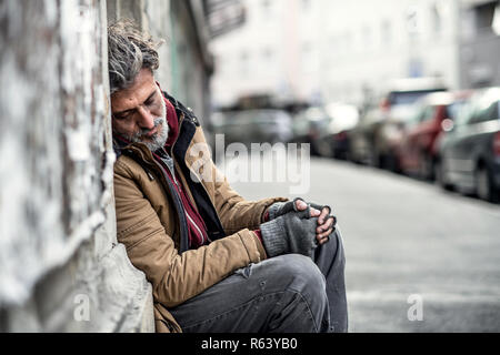 Les sans-abri mendiant homme assis à l'extérieur en ville pour demander de l'argent, don de dormir. Banque D'Images