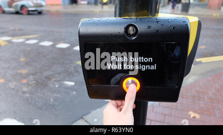 Un pouce gauche appuyant sur un nouveau passage pour piétons sur le bouton signal côté rue, attendant de traverser la route pour aller de l'autre côté. Banque D'Images