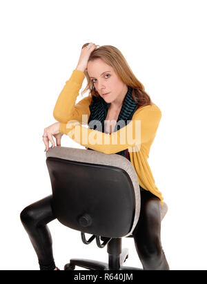 Une jeune femme en pantalon de cuir noir et une veste jaune assis sur une chaise de bureau à la grave, pour isolé sur fond blanc Banque D'Images