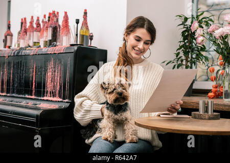 Femme lisant le menu dans le café tenant son chien Banque D'Images
