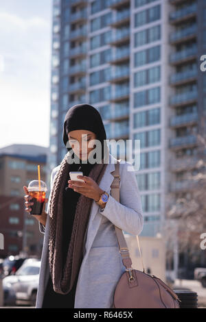 Les femmes ayant de café froid lors de l'utilisation de téléphone mobile dans la ville Banque D'Images