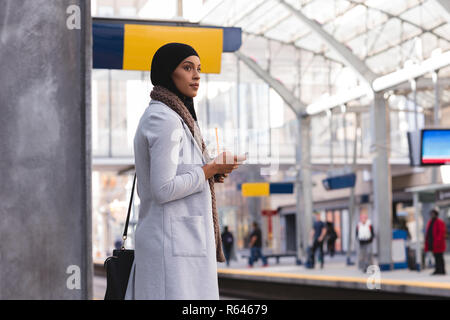 Femme en attente de train lors de l'utilisation de téléphone mobile à la gare Banque D'Images