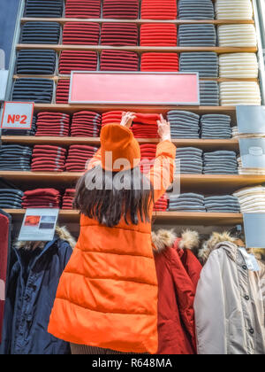 La jeune fille offre sa main pour les vêtements sur l'étagère du magasin. nouveau client tire sur une chose d'une boutique de vêtements. Vue arrière de la femme qui tient la main d'une étagère avec des vêtements affichés en magasin. Banque D'Images