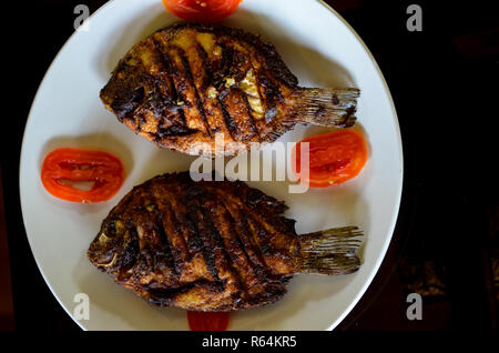 Vue de dessus du plat de poisson frit au Kerala. 2 poissons frits et grillés garnis de tomates sur une plaque en céramique blanche Banque D'Images