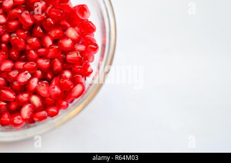 Top close up de graines décortiquées rouge grenade / céréales révélé dans un beau bol en verre à moitié caché sur un fond blanc. Banque D'Images