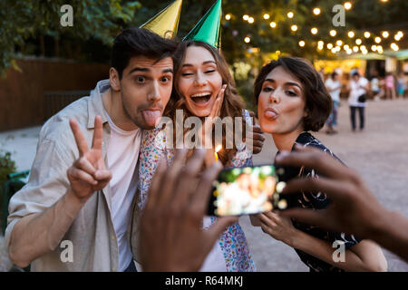 Groupe d'multhiethnic joyeuse fête d'amis avec un gâteau à l'extérieur, prendre photo avec caméra photo Banque D'Images