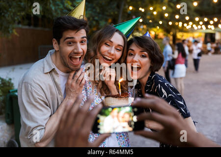 Groupe d'multhiethnic rire amis fête avec un gâteau à l'extérieur, prendre photo avec caméra photo Banque D'Images