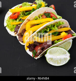 Tacos au boeuf et légumes et de chaux sur une surface noire, vue de côté. Close-up. Banque D'Images