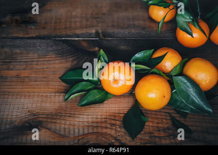 Mandarines mûres avec des feuilles vertes sur un fond de bois foncé, table. Banque D'Images