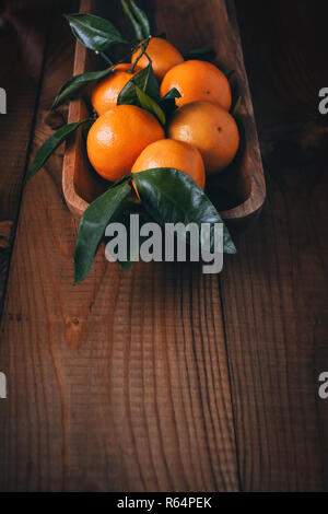 De nombreux mandarins avec des feuilles vertes dans une coupe de bois sur une table en bois sombre. Vintage Banque D'Images