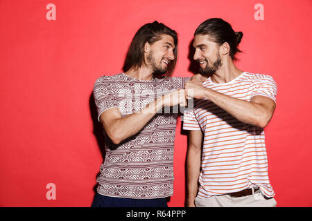 Portrait de deux frères jumeaux souriants isolés sur fond rouge, donnant fist bump Banque D'Images