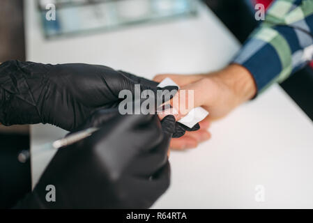 Maître féminin gants noirs dans le polissage des clous pour clients masculins, vue du dessus, les hommes à salon de manucure. Procédure de soins des mains manucure faisant Banque D'Images