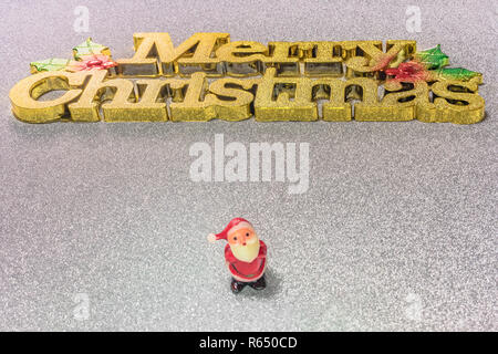 Cute petite figurine du Père Noël sur un background arrière-plan avec la neige mots d'or Joyeux Noël en haut. Banque D'Images