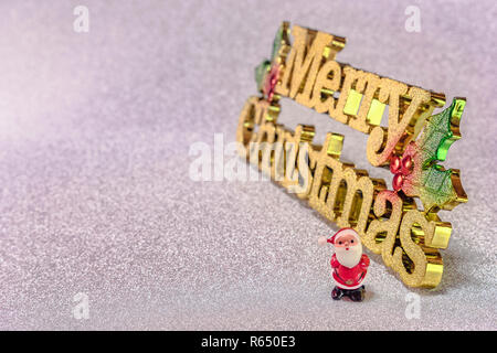 Cute petite figurine du Père Noël sur un background arrière-plan avec la neige mots d'or Joyeux Noël. Banque D'Images