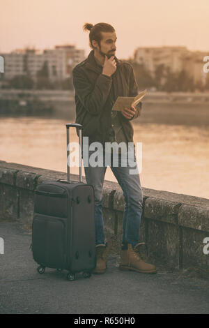 Handsome businessman with suitcase holding plan de la ville et de l'article par la rivière. Banque D'Images