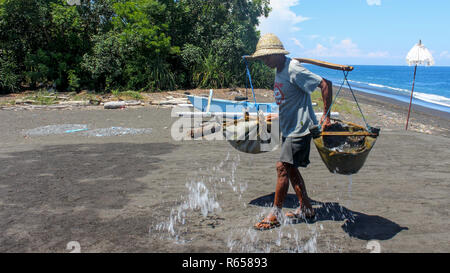 Ancien agriculteur balinais produisant du sel de mer la façon traditionnelle par évaporation. Banque D'Images