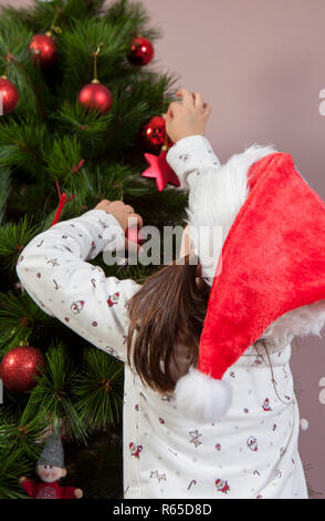 Petite fille décore Arbre de Noël avec une boule rouge Banque D'Images