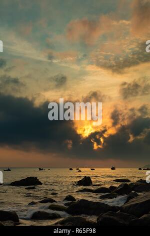 Un orange-feu ciel du matin avec vue sur la mer de Chine du sud à Lam Bay au Vietnam. Avec une côte couverte de roches et de silhouettes de bateaux de pêche. Banque D'Images