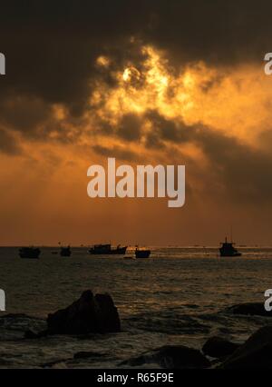 Un orange-feu ciel du matin avec vue sur la mer de Chine du sud à Lam Bay au Vietnam. Avec une côte couverte de roches et de silhouettes de bateaux de pêche. Banque D'Images