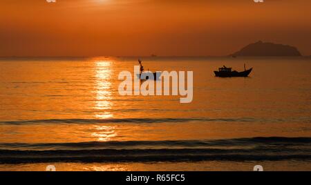 Un orange-feu lever du soleil ciel surplombant la mer de Chine du sud à Lam Bay au Vietnam. Avec un bateau de pêche en silhouette. Banque D'Images