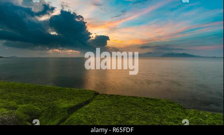 Une vue de la baie de Nha Trang juste avant le lever du soleil avec des roches couvertes de mousse à l'avant-plan. Banque D'Images